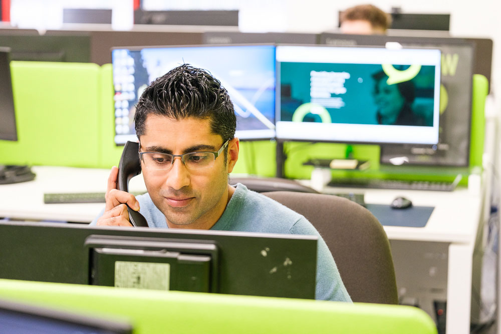 A man project consultant working on a desktop PC while speaking on the phone.