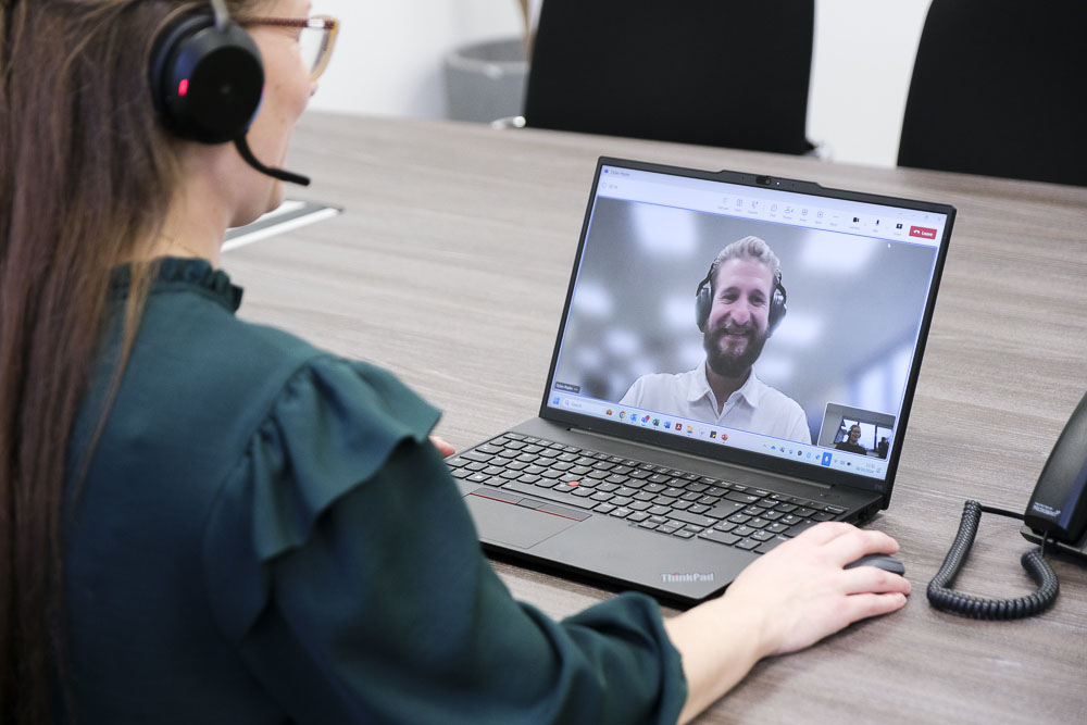 A lady talking to coworker via a video call while sat at a desk.