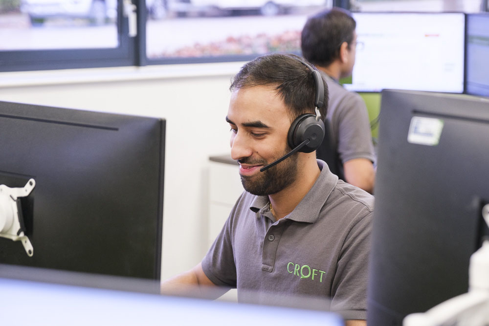 A cyber security expert working at a desktop PC while talking on the phone using a headset.