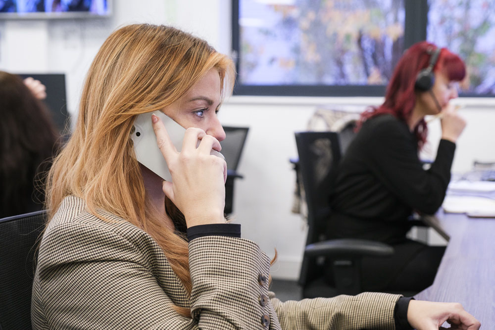 Businesswoman talking on a business mobile phone while working at a desktop PC.