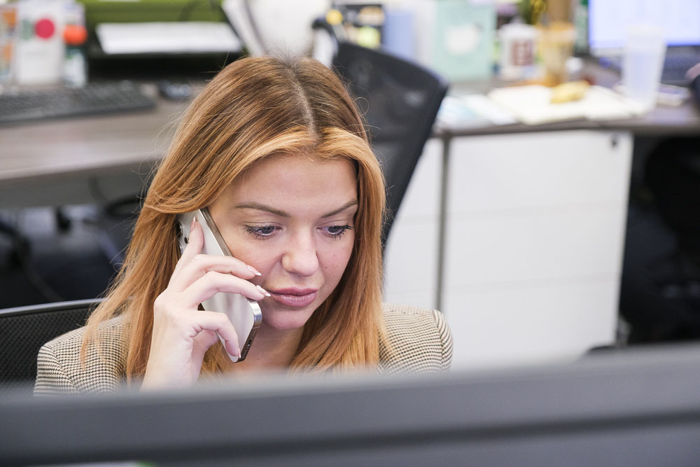 Business lady talking on her mobile phone while working at a desktop computer.