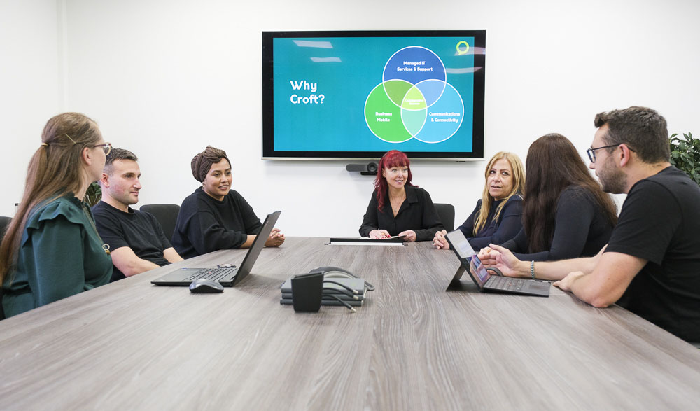 Seven Croft meet the team employees sitting together at our meeting room table in our Hertford office with their laptops.